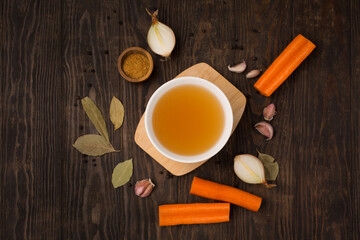 Traditional homemade beef bone broth with vegetable in glass jar on dark rustic wooden background.