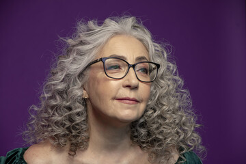 Studio portrait of a smiling elderly woman 60-65 years old with glasses, with gray curly long hair, on a colored background, Concept: stylish pensioners of model appearance, active life,