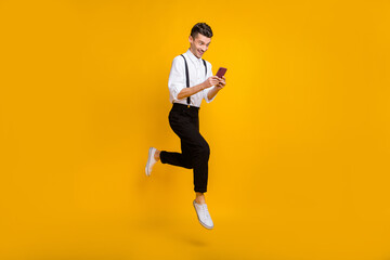 Fototapeta na wymiar Full length body size photo of jumping blogger typing message on cellphone smiling isolated on bright yellow color background