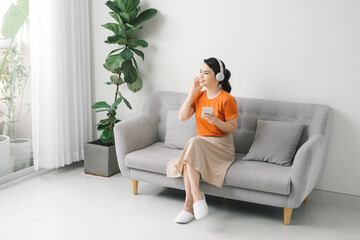 Obraz premium Smiling girl relaxing at home, she is playing music using a smartphone and wearing white headphones