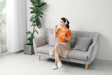 Obraz premium Happy young woman with earphone dancing and listening to music on sofa