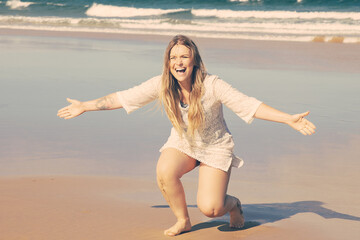 Happy excited woman opening arms and doing squat for catching and hugging child. Wet golden sand,...