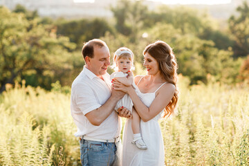 Family enjoying life together in the summer park. People having fun in nature. Happy young family outdoors. Mother, father, child of three smiling while spending free time outdoors