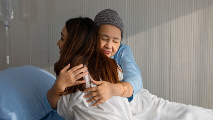 Older Asian woman patient covered the head with clothes effect from chemo treatment in cancer cure process hugging her daughter with love and happy