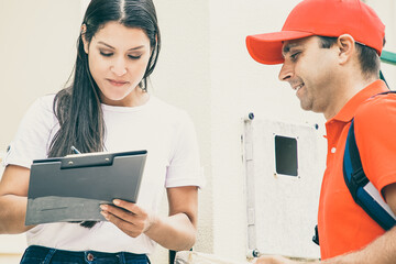 Positive courier in uniform delivering package to customers door. Woman signing for receiving parcel. Shipping or delivery service concept