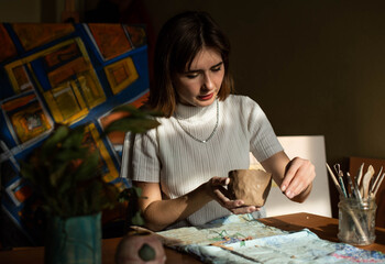 young artist moulding raw clay in art studio. Girl molds from clay sculpture in the artist's studio. Business woman at her pottery store