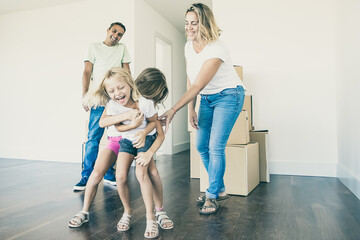 Excited girls tickling each other and laughing. Happy family couple and two kids having fun while...