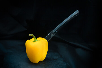 Beautiful steak knife stabbing a yellow bell pepper in black background