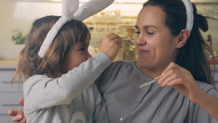 Happy Easter Holiday. Beautiful mother and daughter paint and decorate an egg for a traditional spring dinner at home. Girl with child playing, fooling, drawing easter eggs