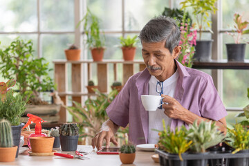 A senior Asian man working in a planting hobby room and drinking coffee with happiness and calm moment. Idea for relaxing and slowly life of older people after retirement