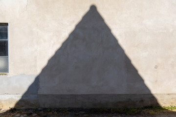 Shadow of a peaked roof on a light roughcast wall of a house next to a window with glass blocks...