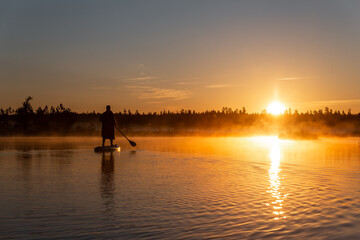 Silhouette of Young woman doing SUP stand up paddle boarding at sunrise in lake. Early summer...