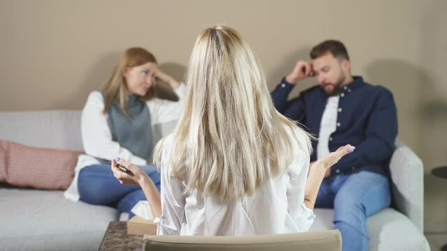 Rear view on blond young psychologist woman looking at quarrelled couple sitting opposite. focus on head of female therapist during therapy session.