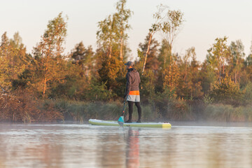 Young athletic man doing SUP stand up paddle boarding at sunrise in swamp. Early summer morning...