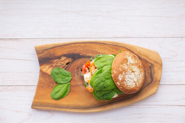 Burger with king prawn, feta cheese and vegetables, on a wooden board