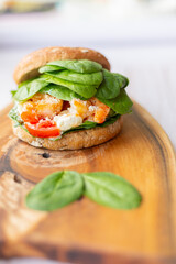 Burger with king prawn, feta cheese and vegetables, on a wooden board