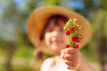 Little girl holding wild strawberry in hand.