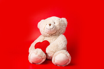 Teddy bear holding a heart on a red background