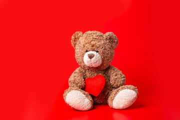 Teddy bear holding a heart on a red background