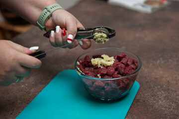 The hands of a woman housewife squeeze the garlic onto the raw chopped beef. Home cooking. Step by step recipe. Garlic press.