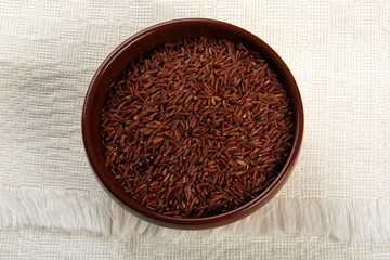 raw red rice in a clay bowl on a light fabric background. uncooked brown wild rice, top view 