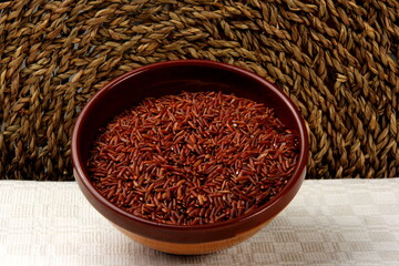 raw red rice in a clay bowl on a light fabric background. uncooked brown wild rice, top view 