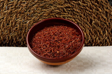 raw red rice in a clay bowl on a light fabric background. uncooked brown wild rice, top view 
