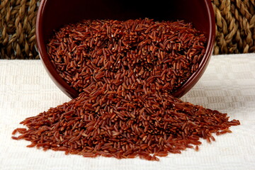 raw red rice in a clay bowl on a light fabric background. uncooked brown wild rice, top view 