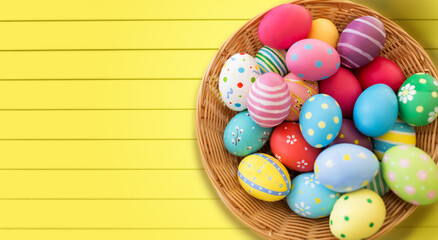 Fototapeta premium easter, holidays and tradition concept - close up of colored eggs in basket over yellow wooden boards background
