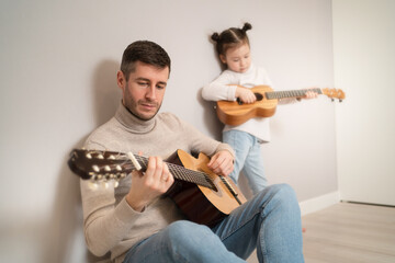 Dad plays the guitar with his daughter. The child learns to play a musical instrument with a tutor. Musical duet of a father with a child