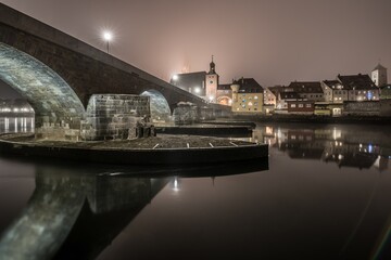Blick zu der steinerne Brücke in Regensburg nachts im Nebel über den Fluss Donau mit dem...