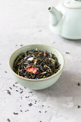 Loose black tea with additives in a bowl on a table with a teapot 