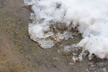 A pile of snow melting on walkway during warm winter. grungy melting snow on an asphalt surface. Ending winter, coming spring idea