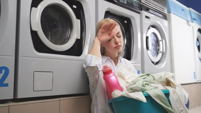 A woman sitting next to a washing machine in a public laundry room, she is tired of waiting for her clothes to be washed in a household washing machine.