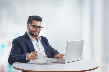 Young man sitting in his office while working on the laptop while drinking coffee. 	