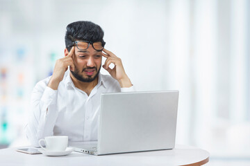 Young man holding his head in frustration due to workload in office. 	