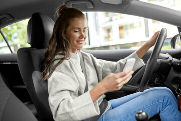 Fototapeta na wymiar safety and people concept - happy smiling young woman or female driver with smartphone driving car in city