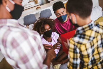 Obraz premium African American parents and cute small kids wearing protective masks spending time together at home. Stop the virus and epidemic diseases.