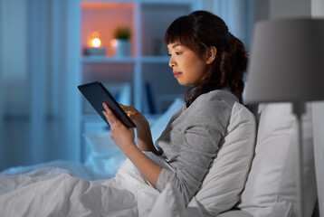 technology, internet and people concept - young asian woman with tablet pc computer lying in bed at home at night