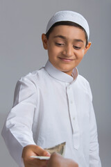 Young Muslim boy wearing cap smiling and giving away money	
