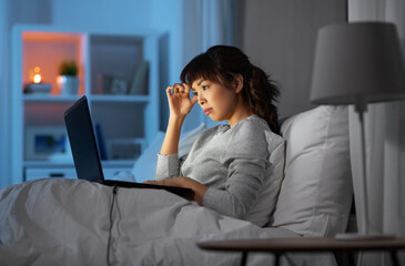 technology, remote job and people concept - stressed young asian woman with laptop computer working in bed at home at night