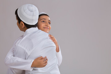 Young Muslim boys with caps hugging each other	