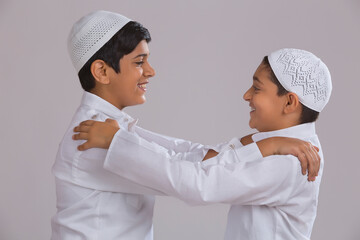 Young Muslim boys with caps looking at each other and smiling	