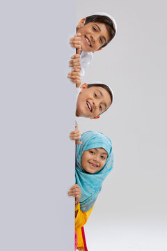 young muslim children peeking out from behind the wall and smiling	