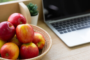 The red apples in the basket are placed on the desk. Apple with a blurred notebook background.