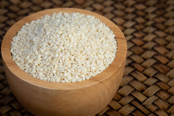 White sesame in a wooden cup placed on a bamboo weave.