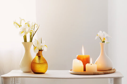 burning candles and spring flowers on wooden shelf in white interior
