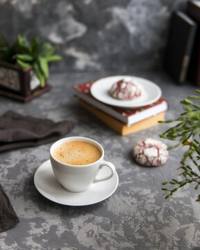Cup of cappuccino in a white mug and red velvet cookies on a dark gray concrete background with books. Selective focuse