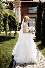 Fototapeta premium bride in a dress standing in a green garden and holding a wedding bouquet of flowers and greenery