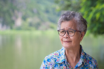 A portrait of an elderly Asian woman smiling and looking at camera while standing in the park. Concept of old people and healthcare